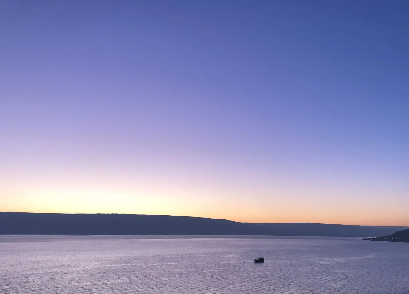 A small boat on calm water at dawn, the sky warming over distant hills.
